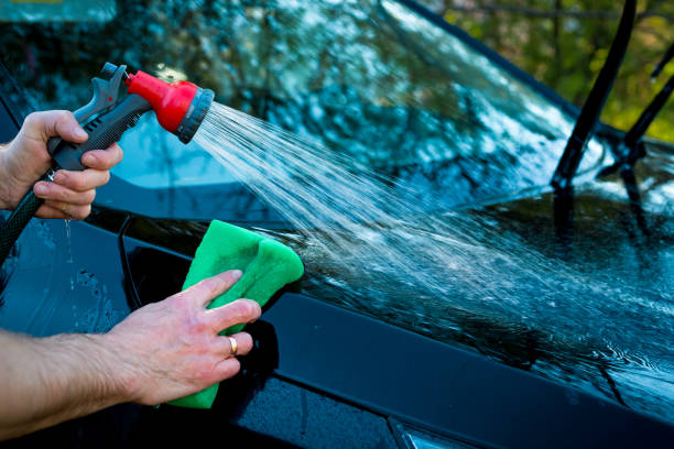 istock driver cleaning auto, automobile windows. Transportation self service, care concept. Car service. A man wash a hood of the car use by sponge and hosepipe with water spray ,car cleansing. 974145992