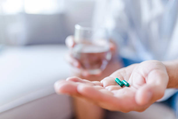 homem toma medicamentos com um copo de água. - capsule close up medicine dose - fotografias e filmes do acervo