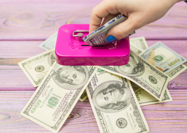 mano de una mujer cae dólares en la hucha. - piggy bank savings pig currency fotografías e imágenes de stock