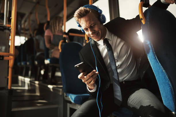 smiling businessman listening to music while riding on a bus - bus riding public transportation businessman imagens e fotografias de stock