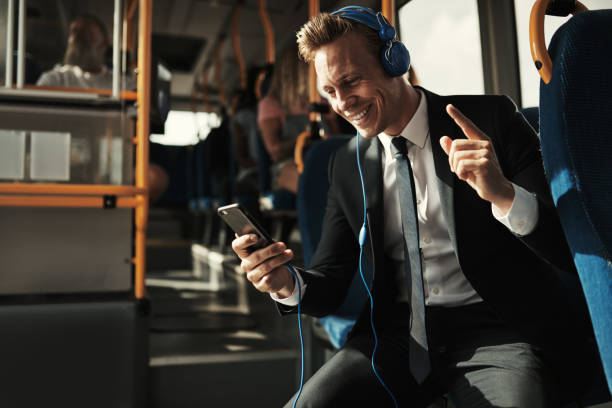 smiling young businessman riding a bus and listening to music - bus riding public transportation businessman imagens e fotografias de stock