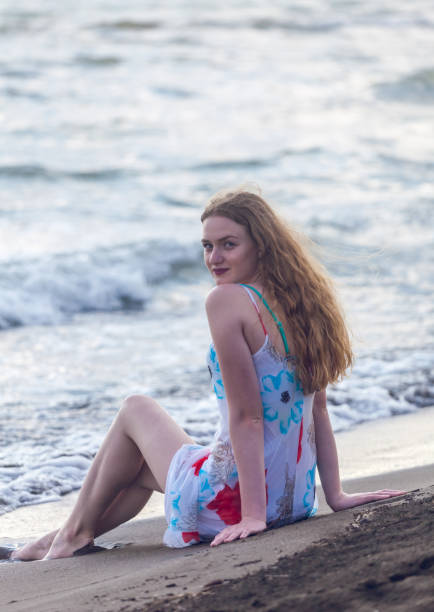 istock Beautiful girl sits on a sandy beach on the seashore 974184174
