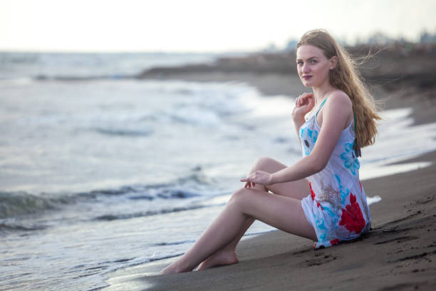 istock Beautiful girl sits on a sandy beach on the seashore 974184474