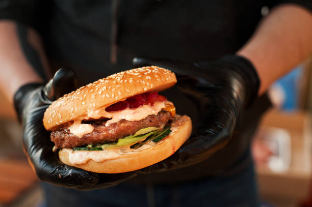 istock Fresh burger cooked at barbecue outdoors. Burger with meat and vegetables close-up, chef unfocused at background. Street fast food. 974199342