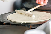 A man spreads batter on a hotplate to make crepes.