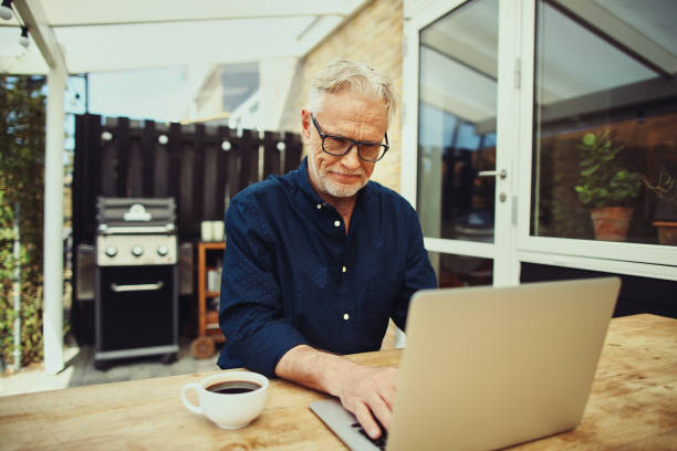 istock Smiling senior man drinking coffee and using a laptop 974226226