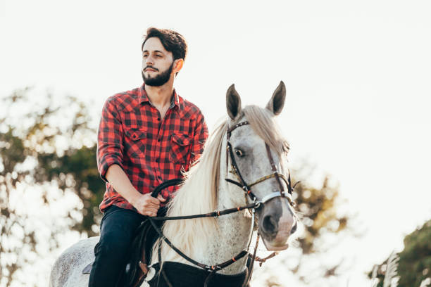 istock Young man riding white horse on the countryside 974232338