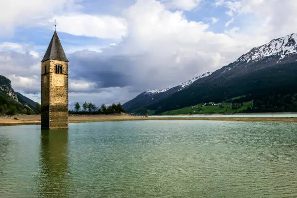 Photo of Church under water, drowned village, mountains landscape and peaks in background. Reschensee Lake Reschen Lago di Resia. Italy, Europe, Südtirol, South Tyrol, Upper Adige, Alto Adige