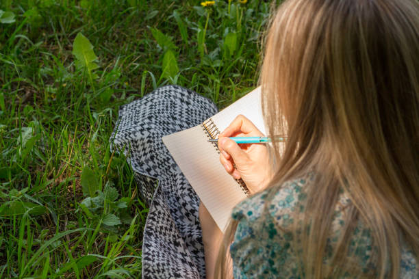istock woman writing in her diary on the grass with flowers. Rear view. 974248422