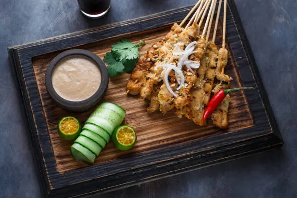 Close view of malaysian chicken skewers - satay or sate ayam with peanut sauce, dark background.
