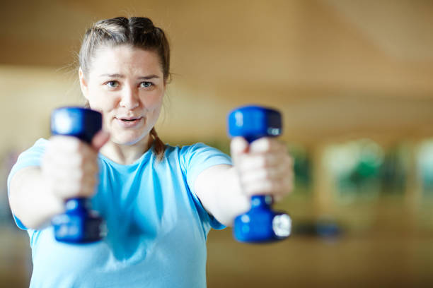 Workout with dumbbells Young female in blue t-shirt doing effective exercise with dumbbells while working out in gym body confidence stock pictures, royalty-free photos & images