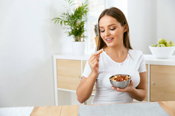 istock Smiling Woman Eating Nuts In Kitchen 974257712