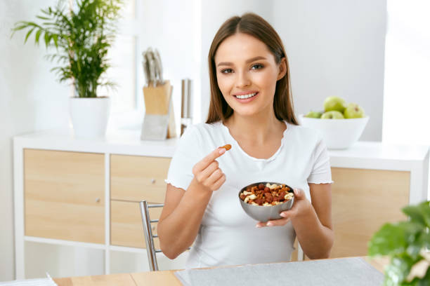 istock Smiling Woman Eating Nuts In Kitchen 974257736