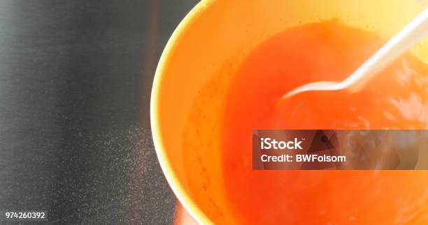 Stirring Orange Gelatin Mix Into A Bowl Of Hot Water With A White Plastic Spoon Stock Photo - Download Image Now