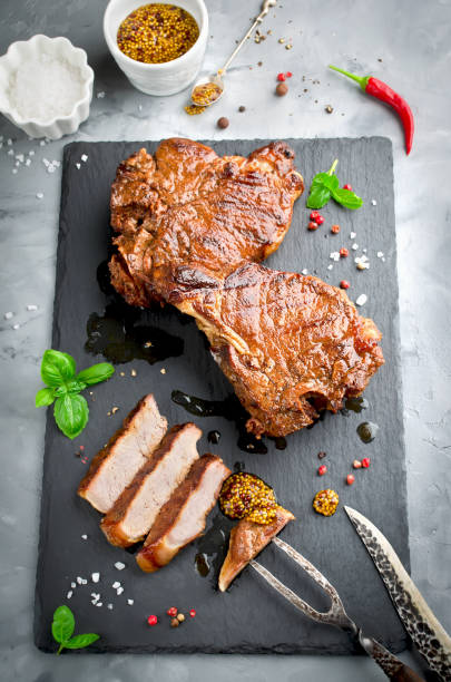 istock Grilled Steak on bone with knife and fork carving set on black stone slate 974265894