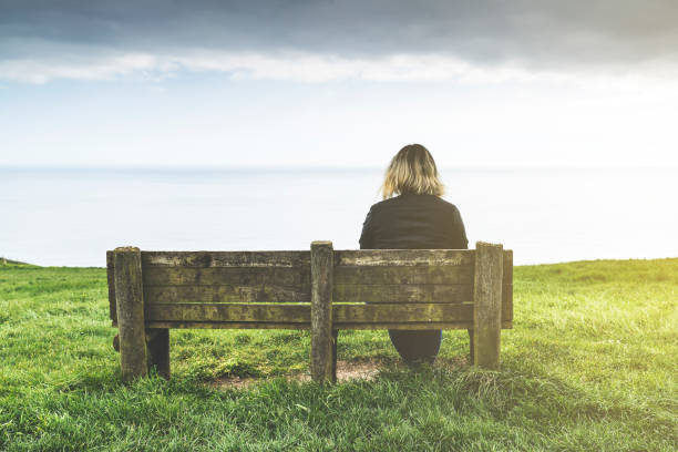 istock Woman sitting on a bench looking at the sea 974270016