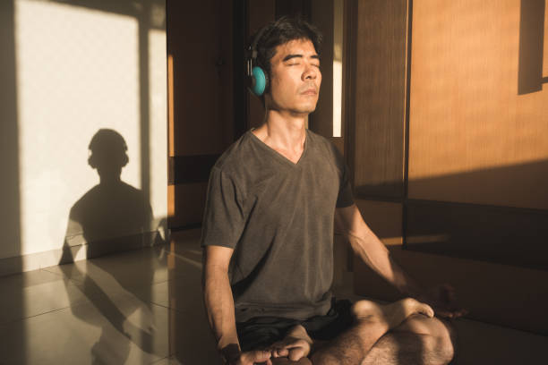 男瞑想ヨガ ロータス ポーズ目閉じた家の床の上に座って - lotus position audio ストックフォトと画像