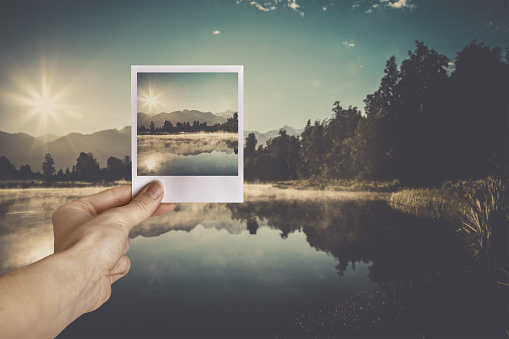 Woman Hand holding instant camera picture at Matheson Lake, New Zealand