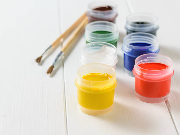 istock Open jars of gouache and brushes on a white wooden table. Creative kit. 974522552