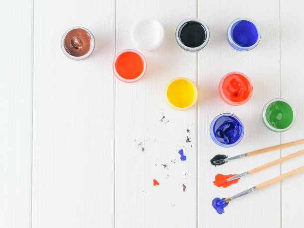 istock Scattered on a wooden table jars of gouache and three multi-colored brushes. Creative kit. Flat lay. 974522558