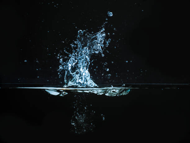 istock Droplet of water dropped into liquid and photographed while making splash on surface. Water splash isolated on dark background. Explosion on the water surface, abstract backgrond. Plash of liquid 974611780