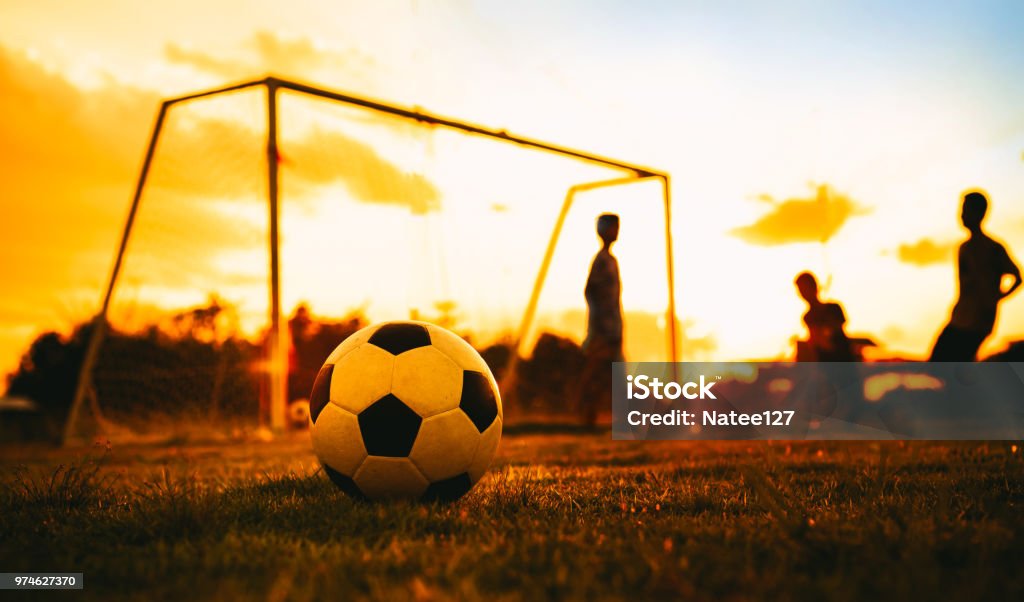 Un cuadro del deporte de acción de un grupo de niños jugando fútbol soccer para ejercicio antes de la puesta del sol. - Foto de stock de Fútbol libre de derechos