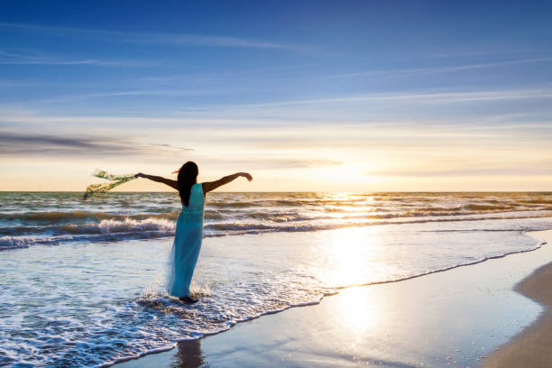 istock Young woman standing on beach with raised arms at sunset 974627868