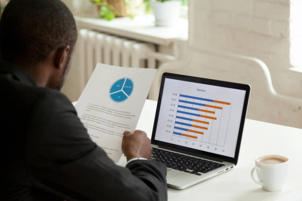 istock Focused black worker comparing financial data on paper and lapto 974640778