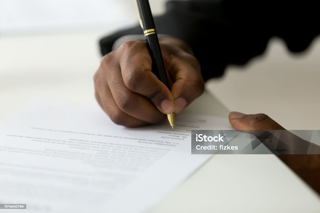 Close up of black worker signing legal documentation Close up of African American worker signing job contract, person being employed at new position, male client putting signature at document in office. Recruiting, promotion, legal documentation concept Signing Stock Photo