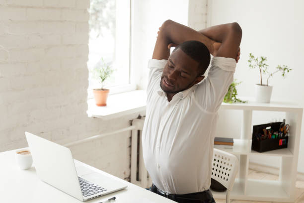 operaio nero esausto che fa ginnastica d'ufficio in sedia al lavoro - yoga men male gymnastics foto e immagini stock