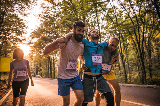 Male athletes helping their injured friend during a marathon race on the road through nature.
