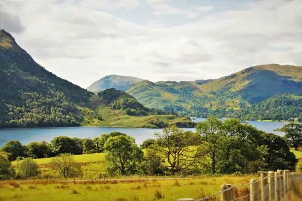 A photo of a blue lake in the lake district with a fence in the foreground, and mountains in the background.