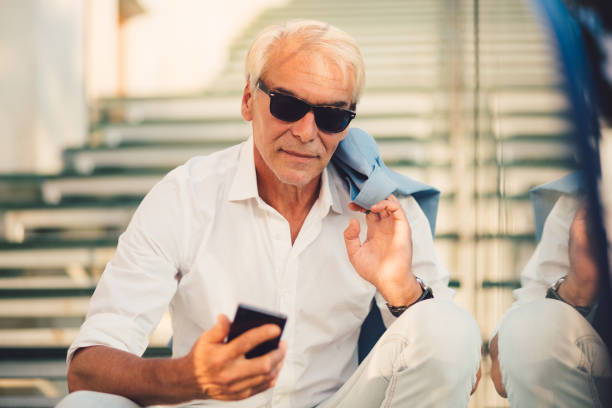 istock Senior businessman sitting at the steps and texting 974667630