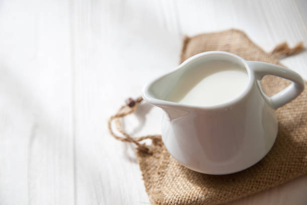 istock White milk pitcher on a white wooden background. 974675926