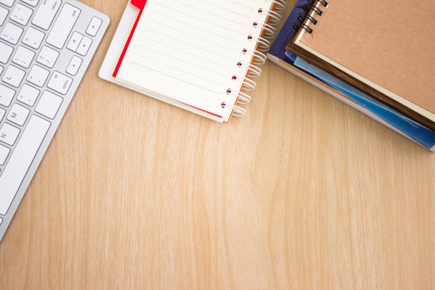 istock blank paper book on wood table / paper with copy space, keyboard, notebook on a wood desk, view from above / for your text or message / top view 974676004