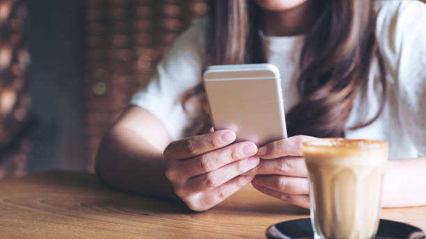 istock Closeup image of a woman holding , using and touching a smart phone while drinking coffee 974676356