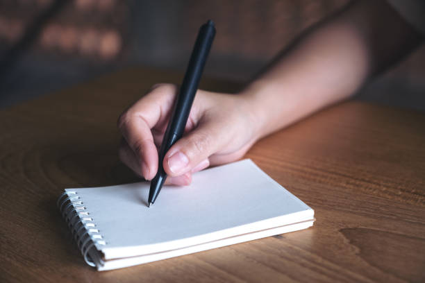 istock Closeup image of a hand writing down on a white blank notebook on wooden table 974676920