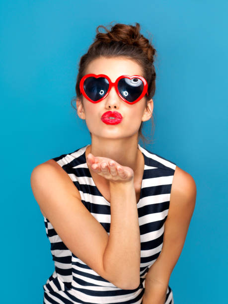 This goes out to you Studio shot of a beautiful young woman wearing sunglasses while posing against a blue background blowing a kiss stock pictures, royalty-free photos & images