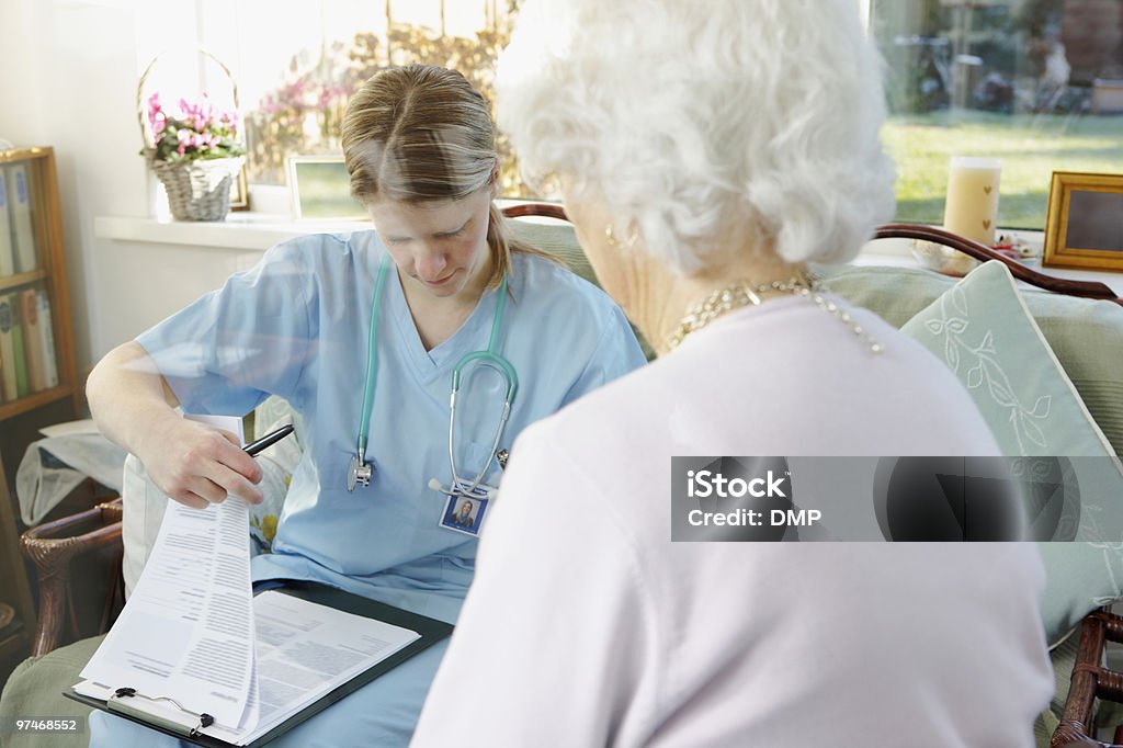 Medico scrivendo medical report per donna anziana in una casa di cura - Foto stock royalty-free di Accudire