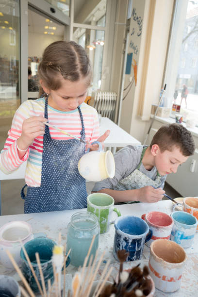 istock Kids concentrating on painting  pottery cups 974690800