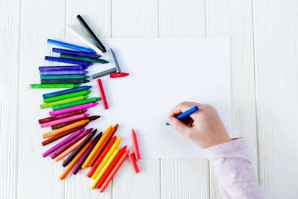 útiles escolares para dibujar sobre la mesa: papel y lápices de colores. un niño sostiene un lápiz en sus manos - sorteo de partidos fotografías e imágenes de stock