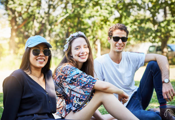 istock Three young friends sit on a row on park lawn 974714170