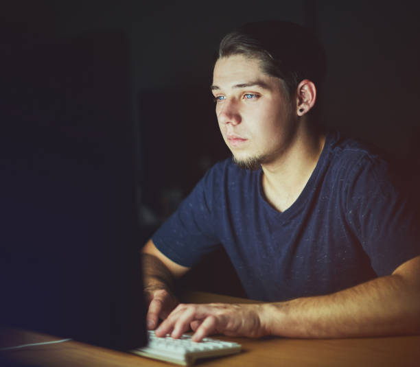istock Young man sitting in dark busy with his computer 974716286