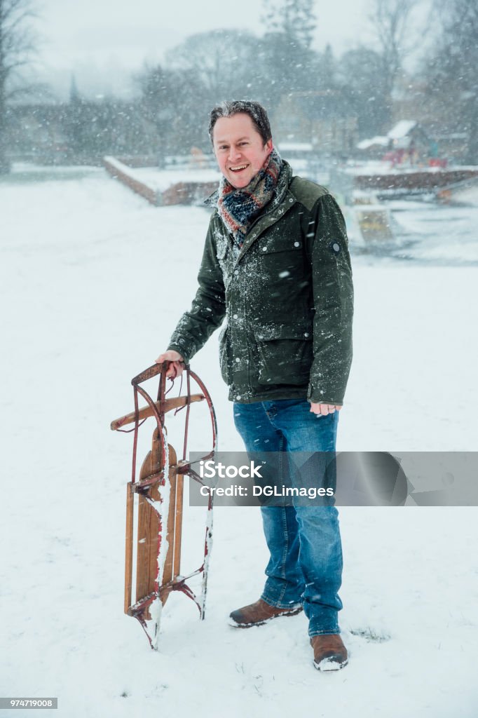 Potrait of Man with Sleigh Mature man is smiling for the camera while standing outdoors in the snow, holding a sleigh. 40-49 Years Stock Photo