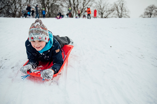 Little boy is lying on a sled, going down a hill in the snow.