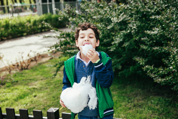 Cute little child eating white cotton candy in the park Happy child eating cotton candy at carnival in park child cotton candy stock pictures, royalty-free photos & images