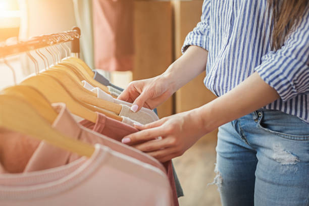 Smiling girl bying clothes in showroom Unrecognizable woman choosing clothes on rack in showroom. Sale, fashion and consumerism concept, crop boutique stock pictures, royalty-free photos & images