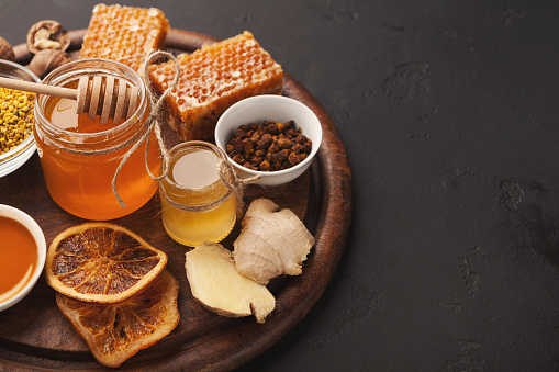 Honey assortment, closeup. Glass jar, honeycombs, pollen bowl, nuts, ginger, mint and dry oranges. Sweet background, wallpaper. Natural medicine concept, copy space