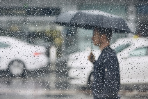 Rain in city. Young man holding umbrella walking in the street. Selective focus on  raindrops on the window.