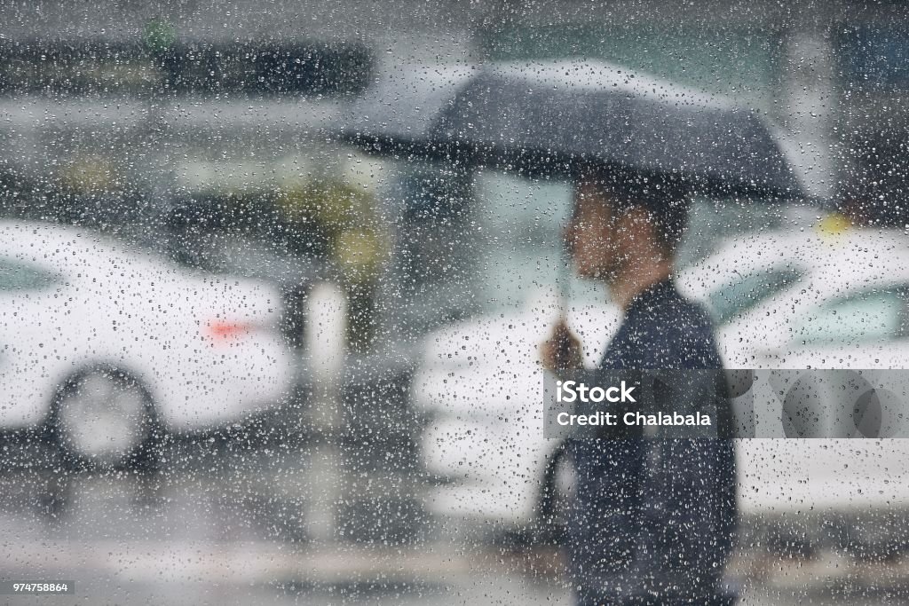 Rain in city Rain in city. Young man holding umbrella walking in the street. Selective focus on  raindrops on the window. Rain Stock Photo